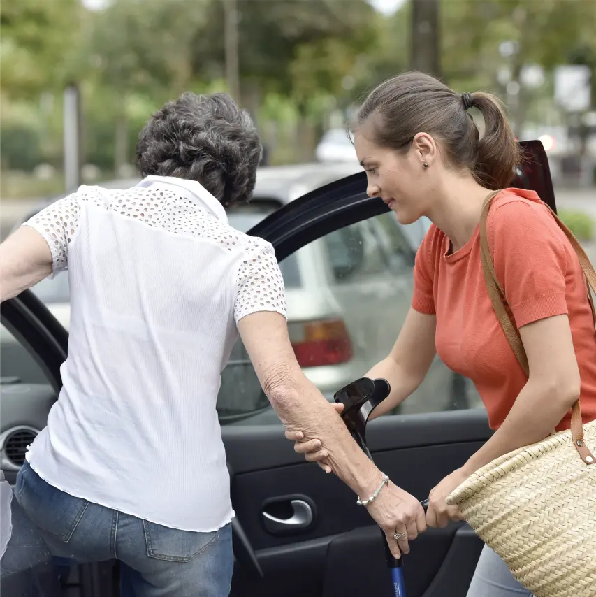 Young, White female volunteer helping senior Asian woman into her car