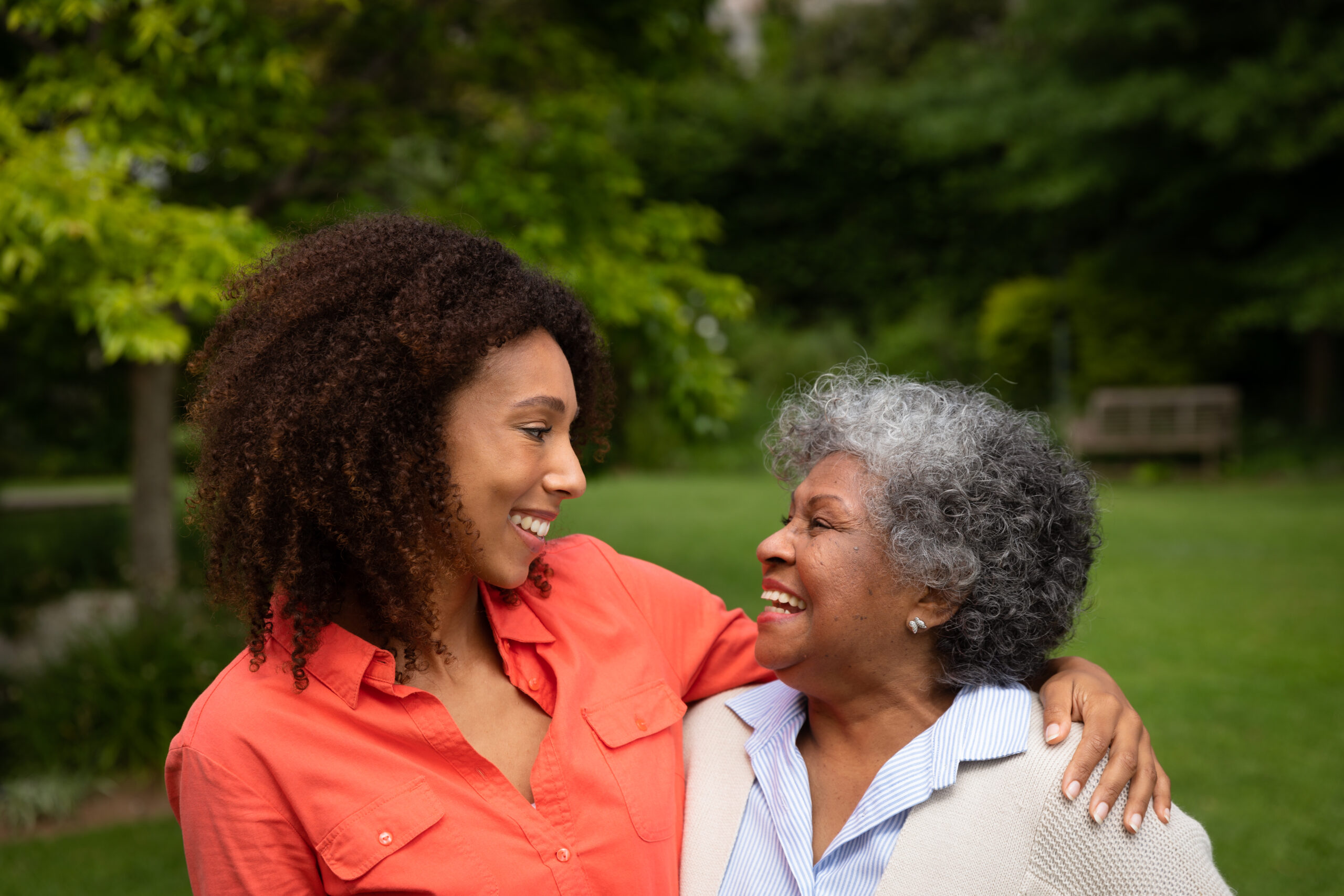 Black adult daughter and her elderly mother standing outside smiling at each other